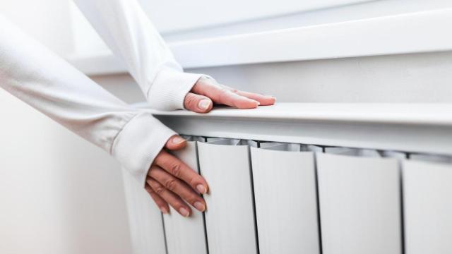 Mujer calentando las manos sobre un radiador.