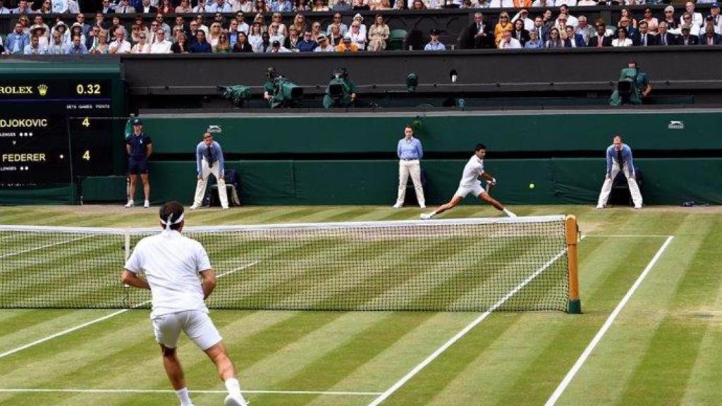 Un partido de Wimbledon entre Djokovic y Federer bajo la supervisión de los jueces de línea al fondo de la pista.