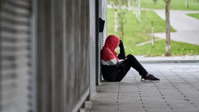 Un joven se sienta solo en mitad de la calle.