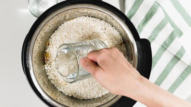 Una persona echa agua en una olla para cocer arroz