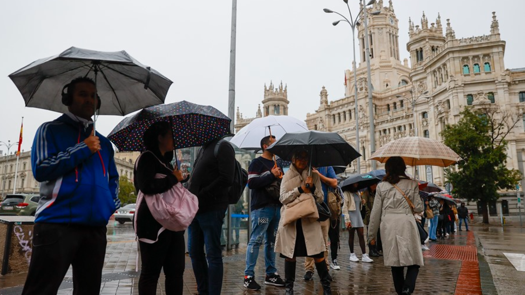 Personas se resguardan de la lluvia en la plaza de Cibeles de Madrid.