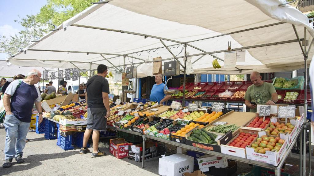 Varias personas compran en un puesto de frutas en el mercadillo de Plaza Elíptica, en Madrid (España).