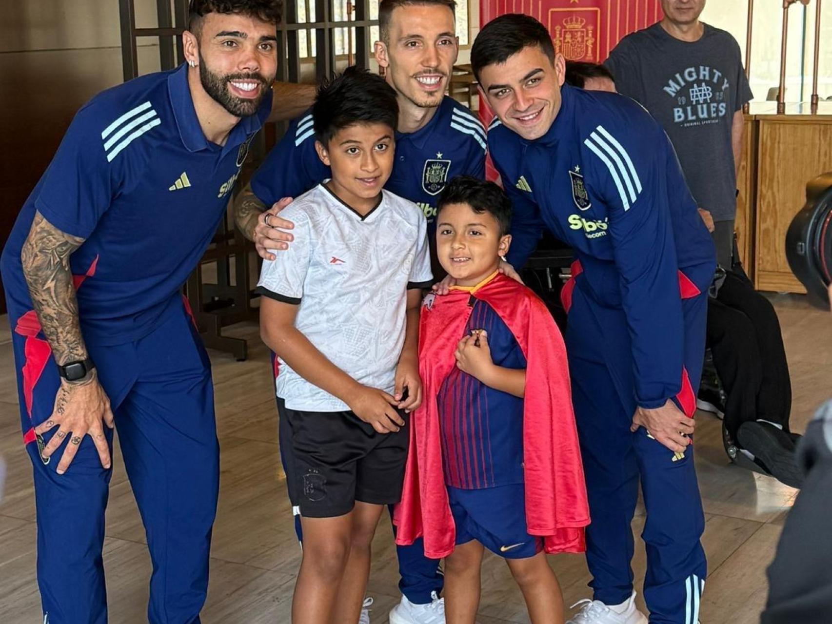 Los internacionales por España, David Raya, Grimaldo y Pedri, posando con un sonriente Luciano, de 7 años, vestido con su capa de 'Super Lucky', junto a su hermano mayor, Juan, de 9 años.