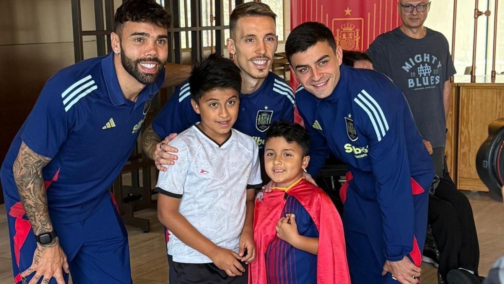 Los internacionales por España, David Raya, Grimaldo y Pedri, posando con un sonriente Luciano, de 7 años, vestido con su capa de 'Super Lucky', junto a su hermano mayor, Juan, de 9 años.