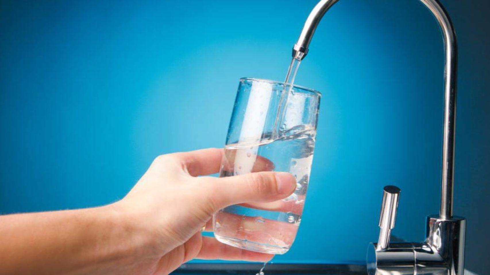 Una persona llenando un vaso de agua en el grifo.