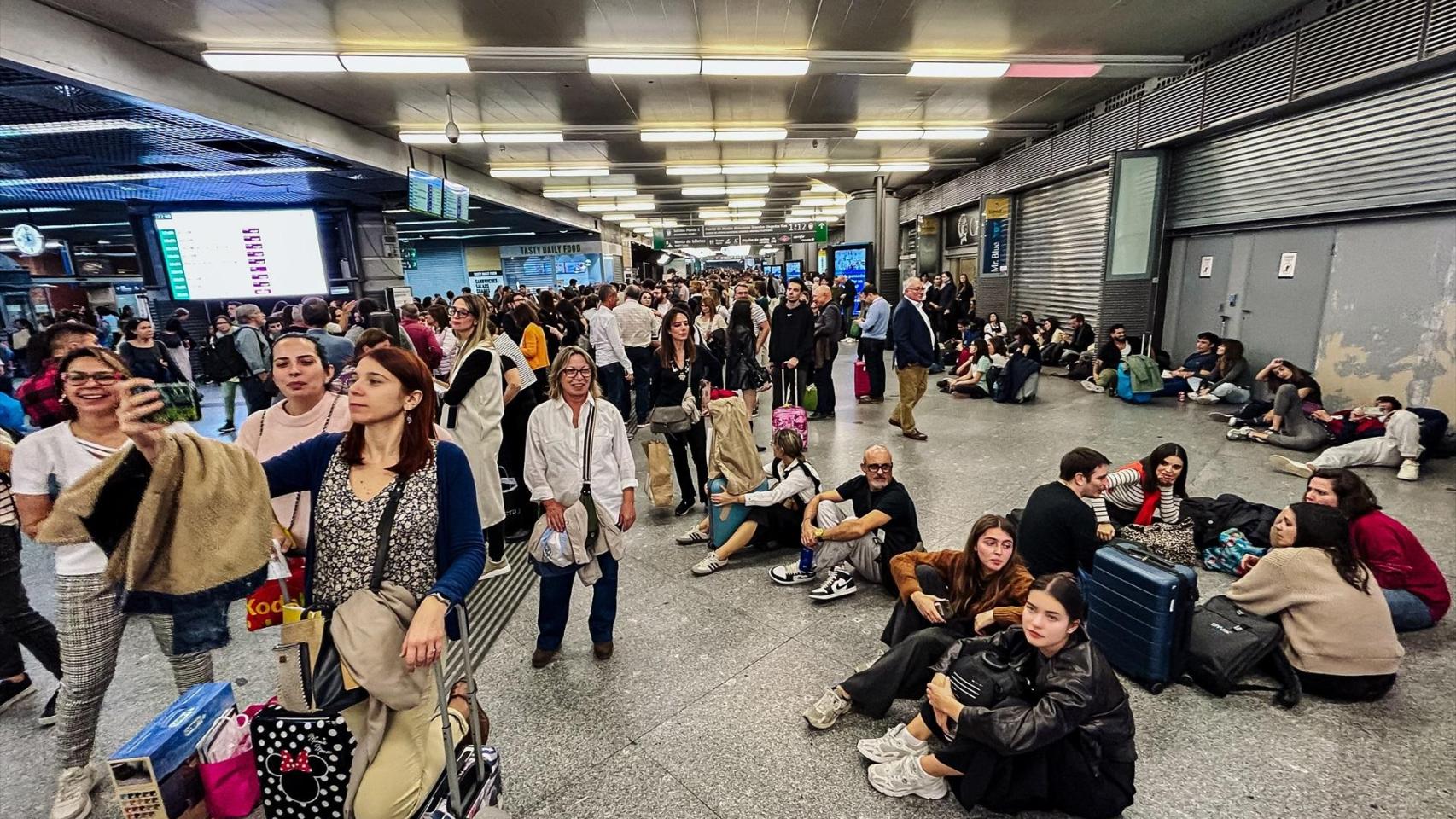 Un grupo de personas espera en el suelo en la estación de Atocha.