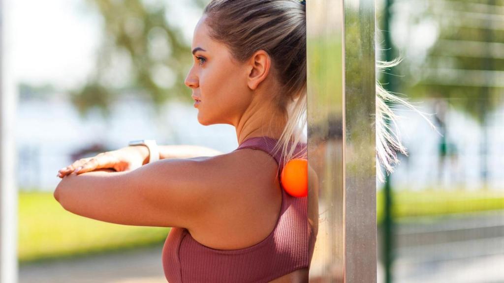 Mujer con ropa de deporte dándose un masaje con una pelota.