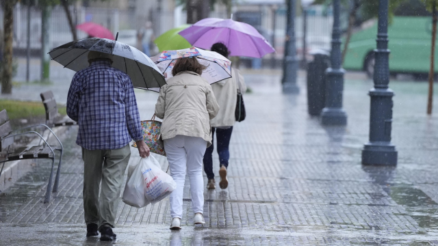 Varias personas caminan bajo la lluvia.