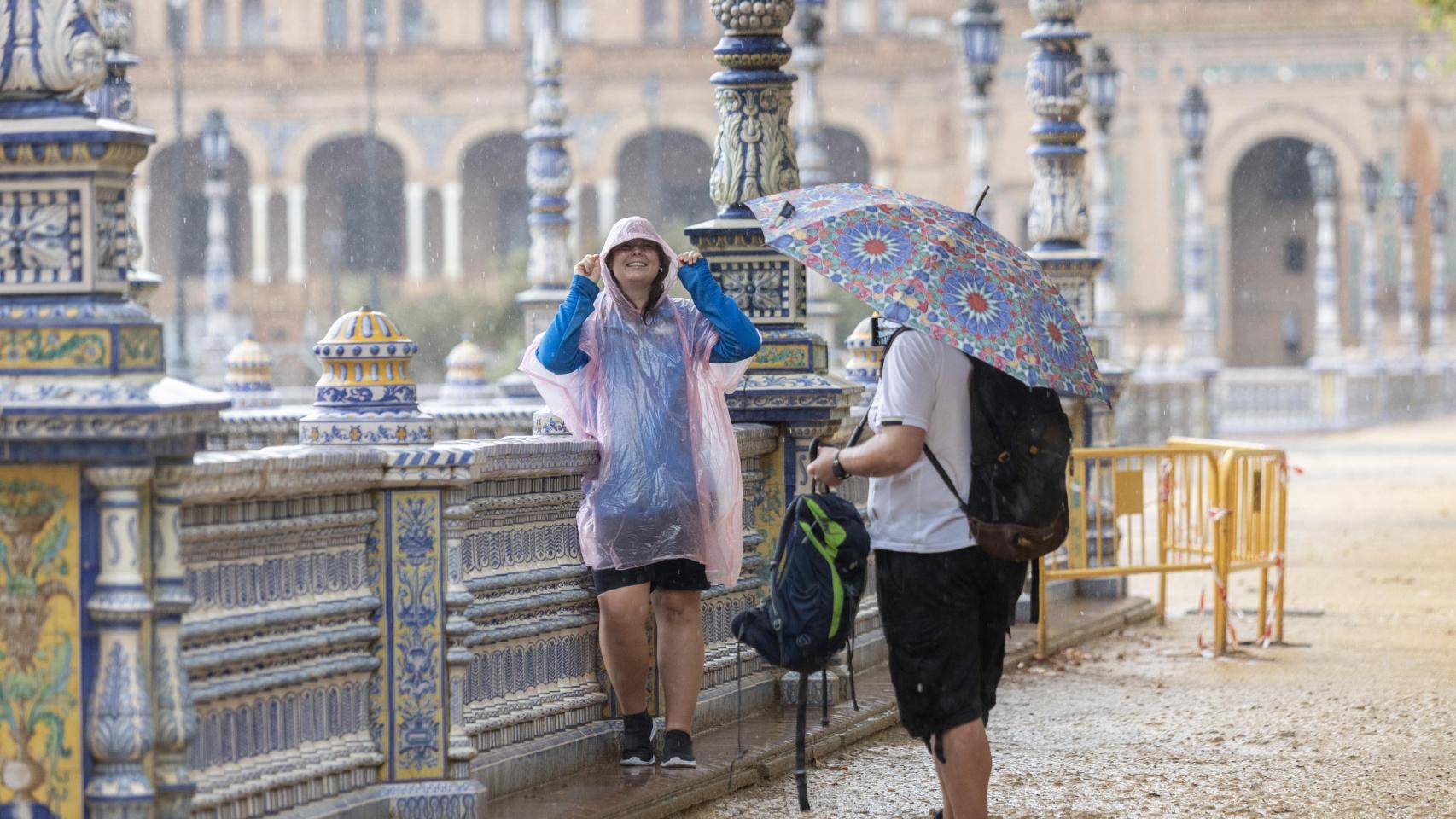 Turistas se protegen de la lluvia en la Plaza España de Sevilla.