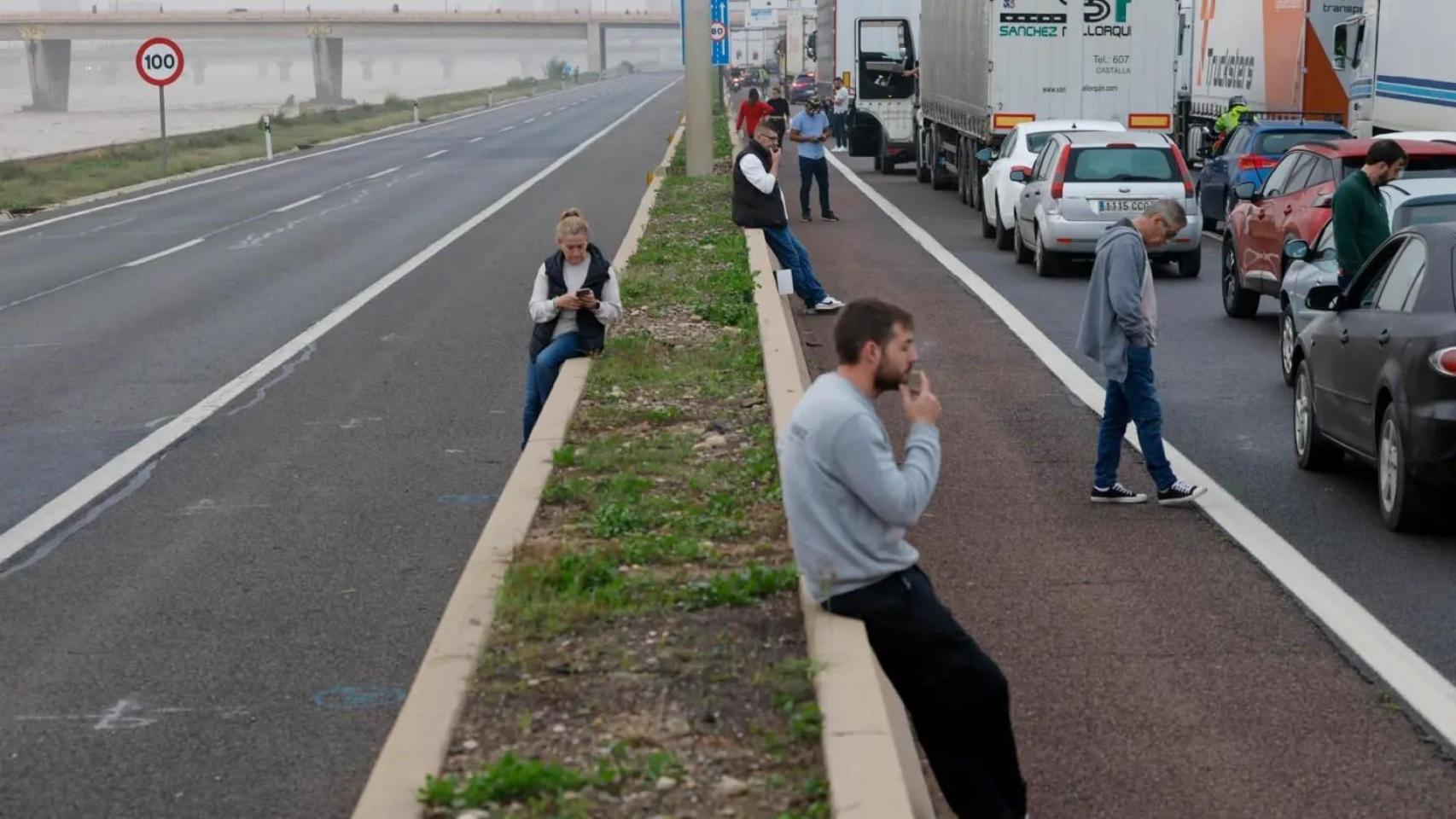 Conductores aguardan junto a sus vehículos en la V-30 junto al nuevo cauce del Turia de Valencia, durante la mañana de este miércoles en la que la red principal de carreteras permanece cortada en varios puntos EFE/Biel Aliño