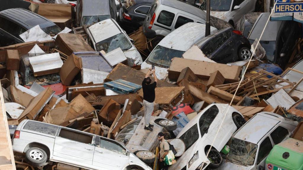 Un hombre fotografía la montaña de coches apilados tras la riada, en una calle de Paiporta, donde ha habido 45 fallecidos.