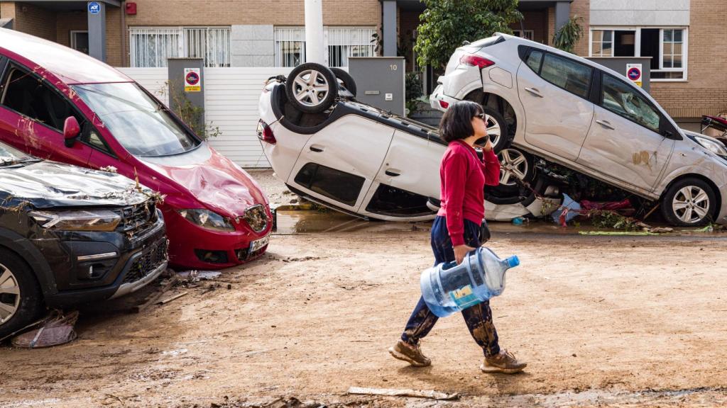 Una mujer camina frente a varios vehículos accidentados en la Calle José Capuz, en el centro de Paiporta.