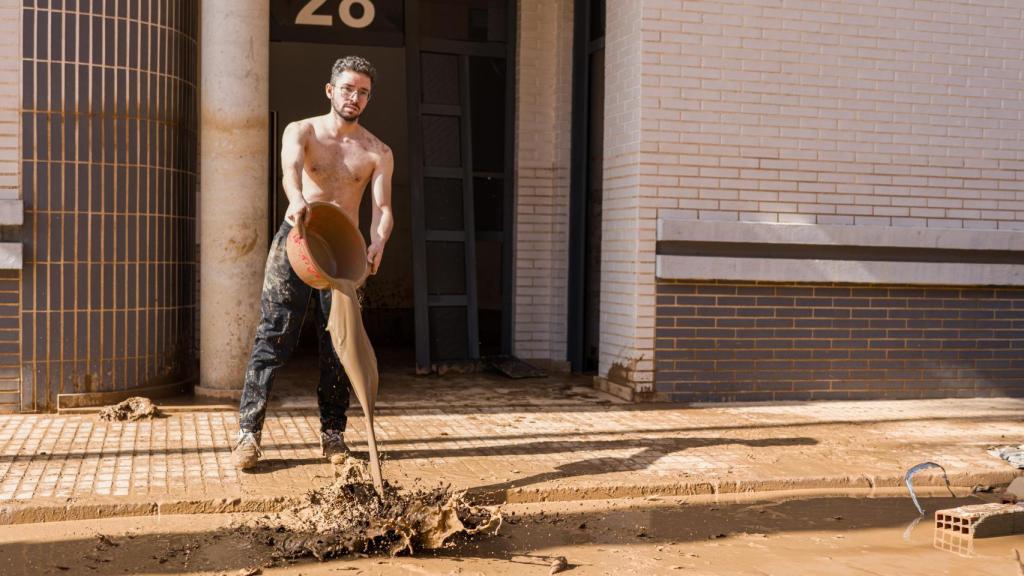 Adrián vacía en la calle un barreño lleno del agua que intenta extraer de su casa.