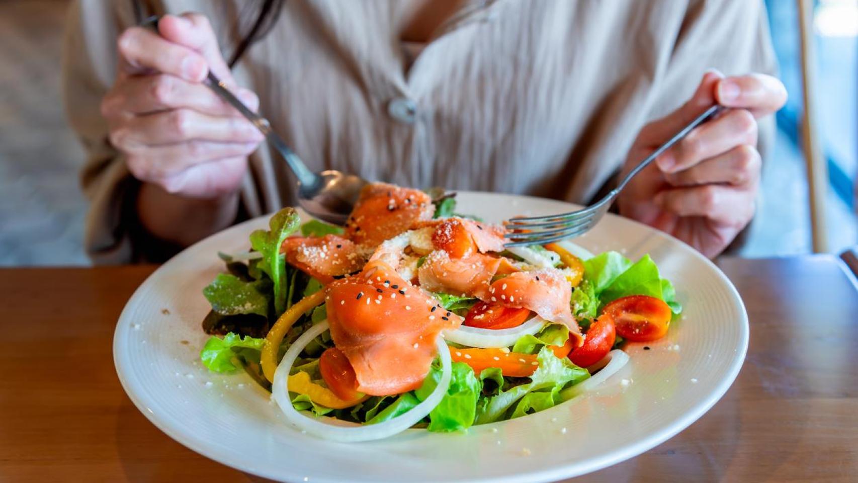 Mujer comiendo salmón con verduras.