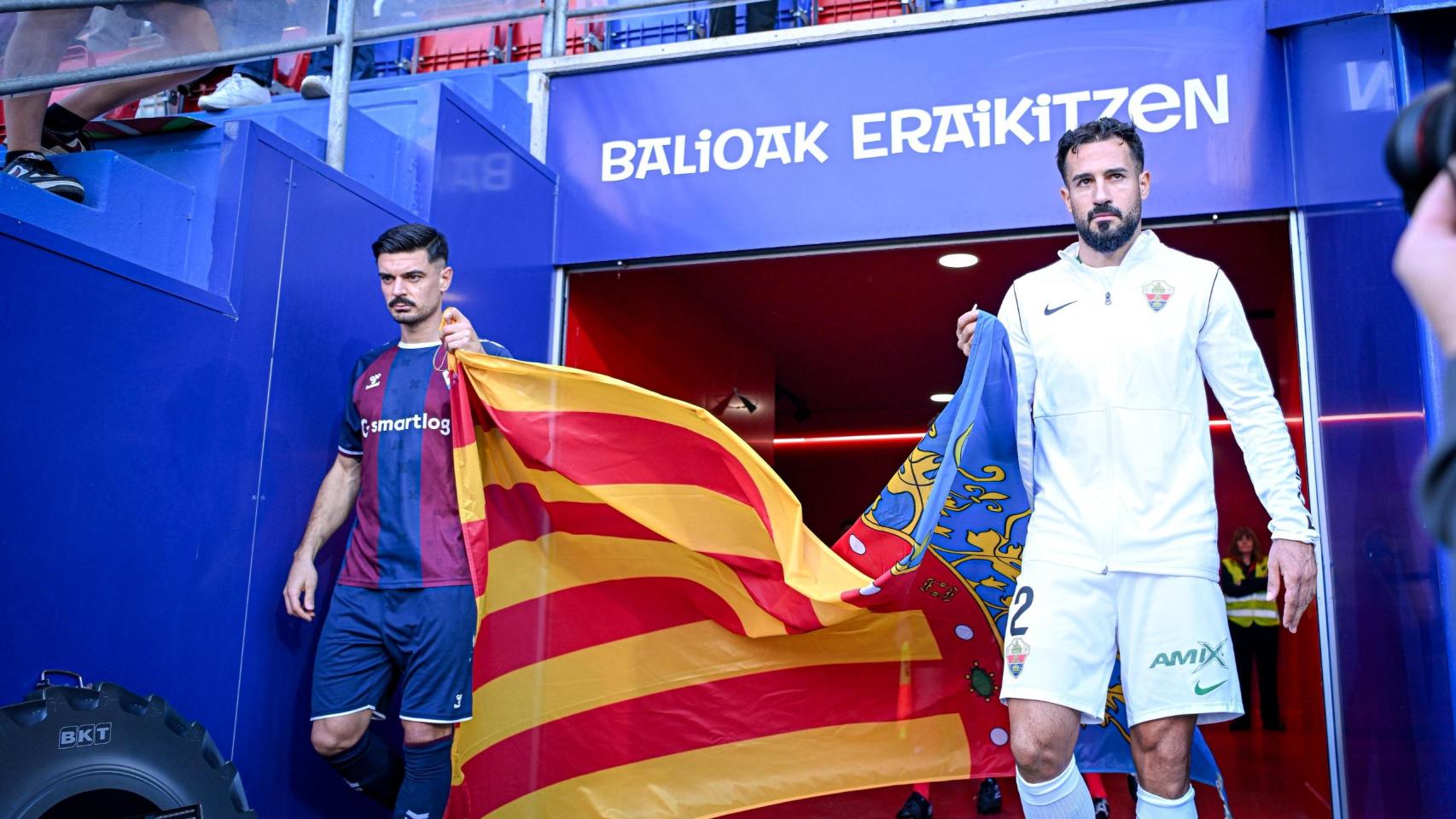 jugadores del Elche y del Eibar posan antes del partido con la bandera de la Comunidad antes del partido.