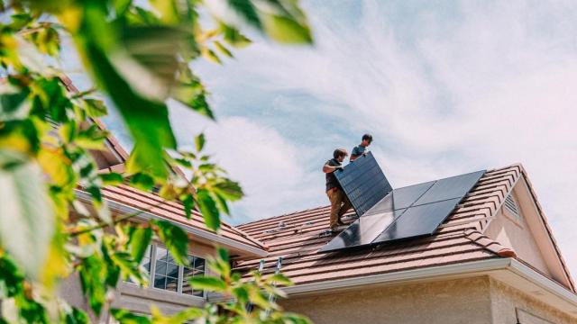 Jóvenes instalan paneles fotovoltaicos en el tejado de una vivienda.