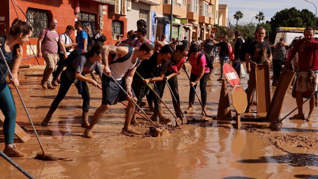 Fotografía de voluntarios y vecinos colaborando por limpiar las calles de los pueblos afectados por la DANA en Valencia.