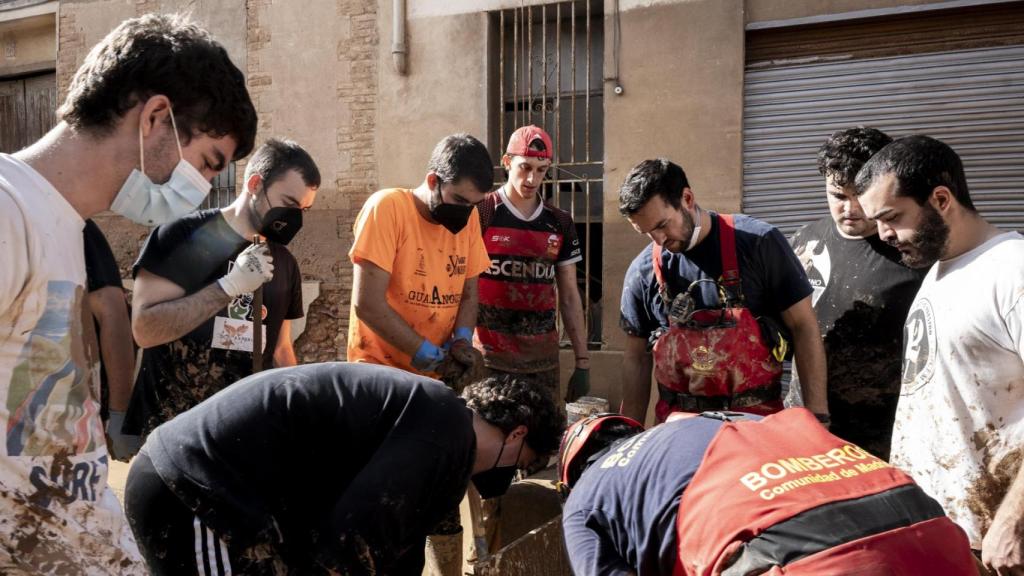 Grupo de jóvenes ayudando a los Bomberos de Madrid a desatascar una alcantarilla en Llocnou.