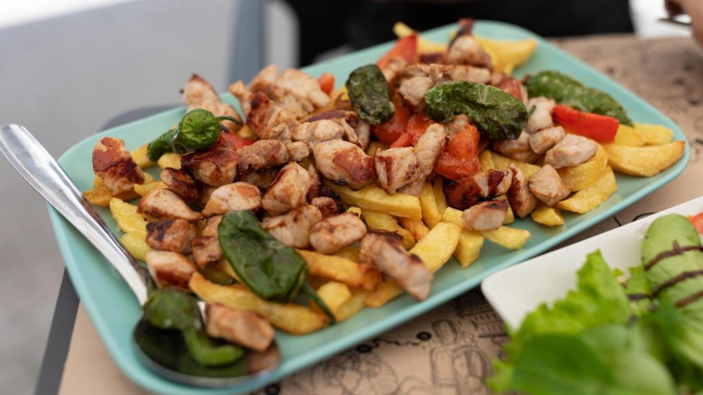 Un plato de raxo con patatas y pimientos de Padrón