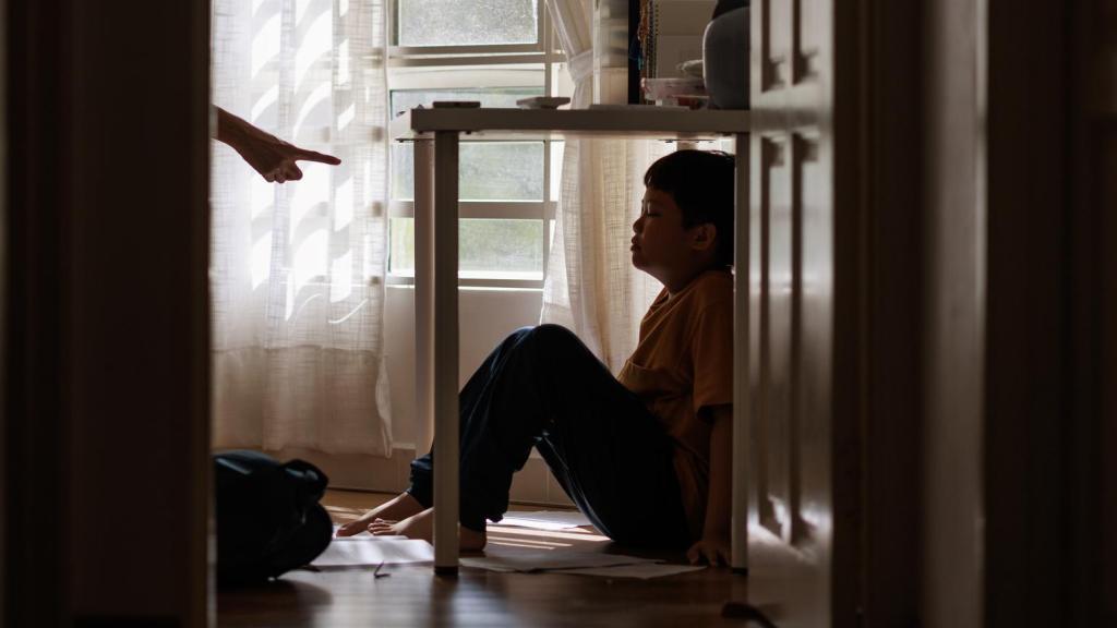 Imagen de un niño refugiándose debajo de una mesa por enfado de sus padres.