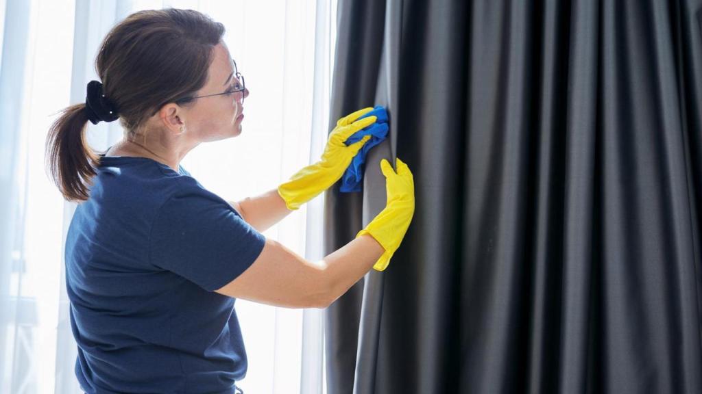 Una mujer limpiando cortinas.