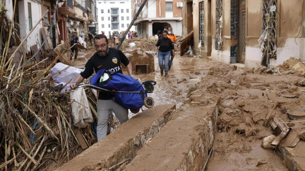 Un hombre camina por una calle arrasada en Paiporta, con restos de cañas arrastradas por la riada.