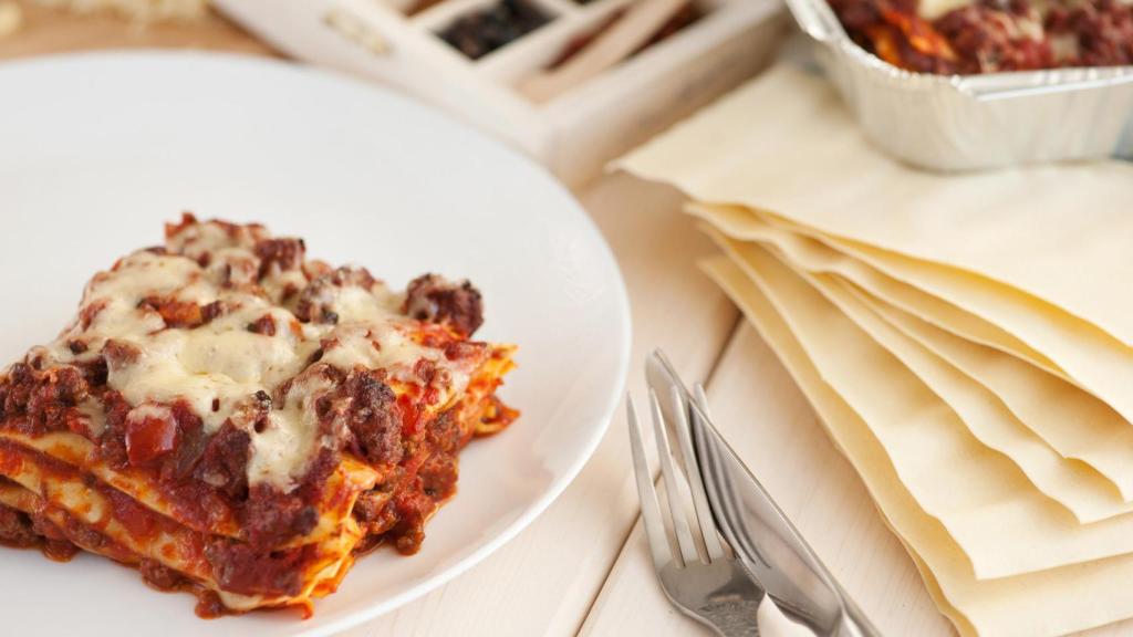 Una lasaña cocinada y unas placas de lasaña de pasta seca.