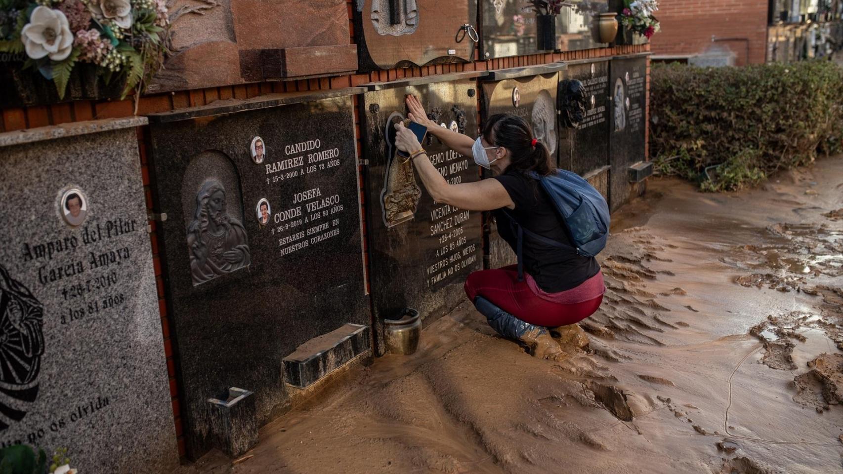 Una mujer llega a la tumba de sus abuelos tras pasar al cementerio de Alfafar entre el barro.