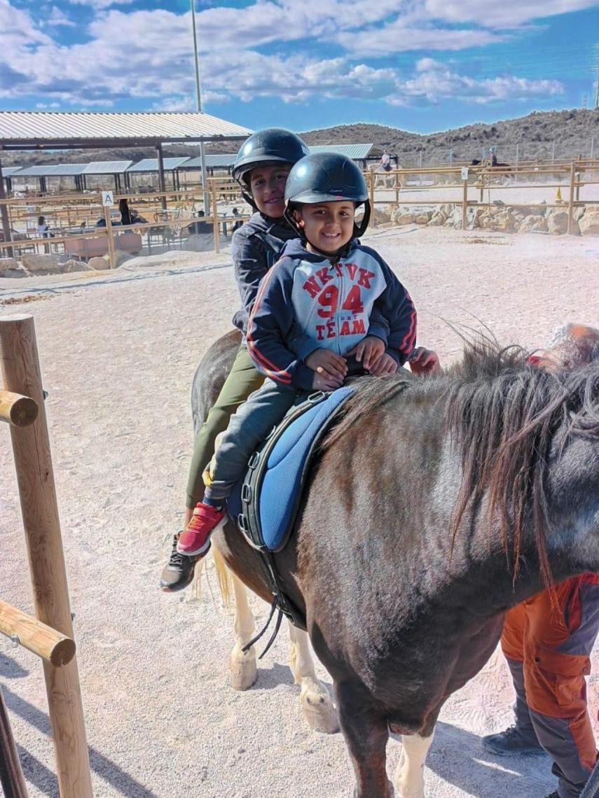 Luciano, sonriente, junto a su hermano mayor, Juan, montando a caballo en un refugio de animales.