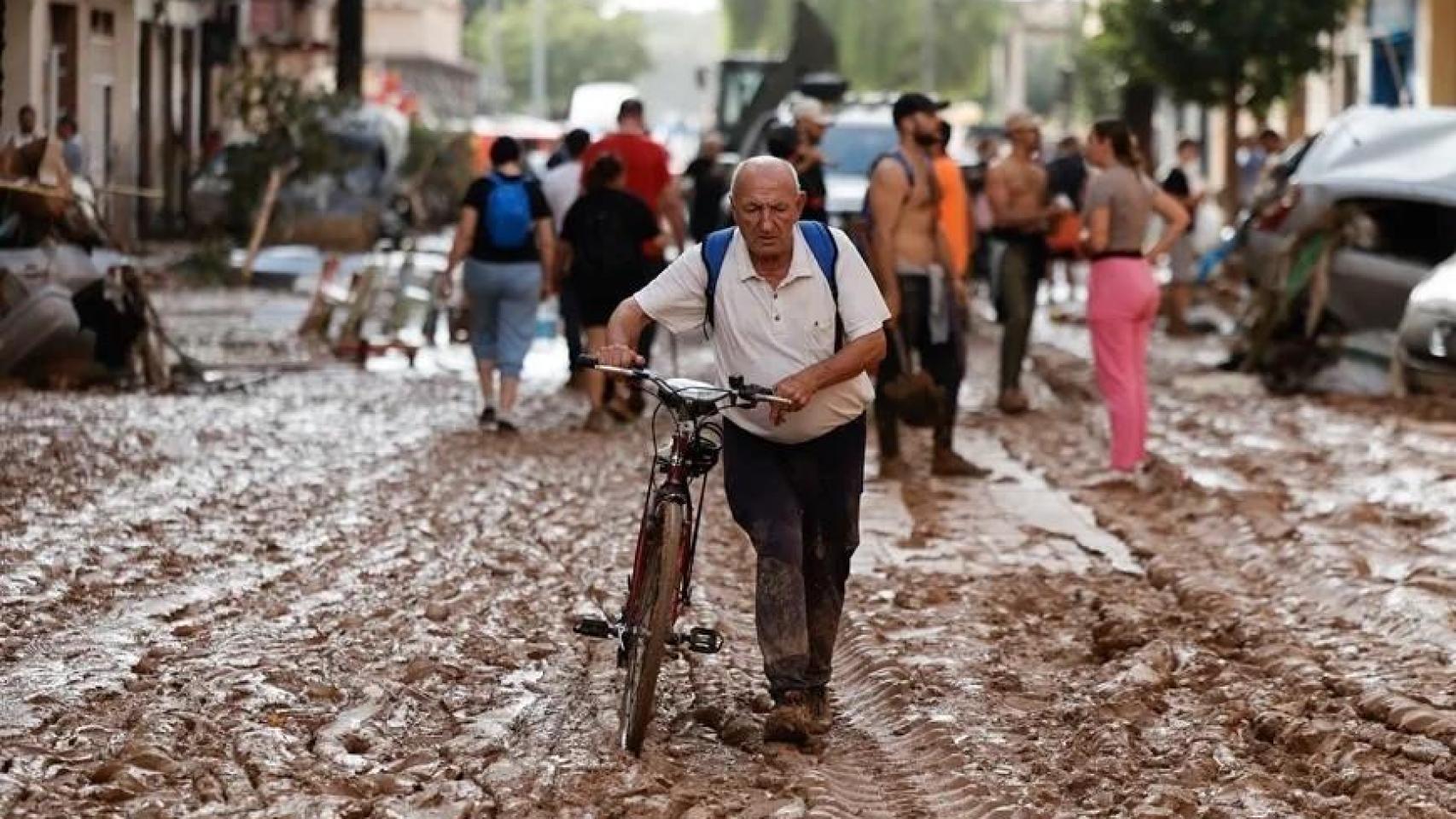 Un vecino de Paiporta atraviesa con su bicicleta una calle cubierta de barro. EFE/Biel Aliño