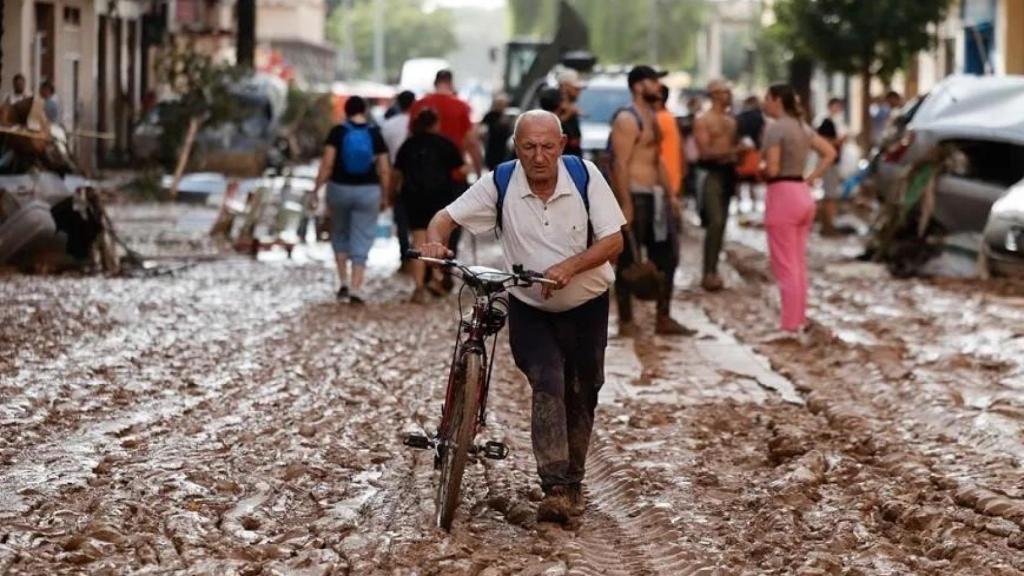 Un vecino de Paiporta atraviesa con su bicicleta una calle cubierta de barro. EFE/Biel Aliño