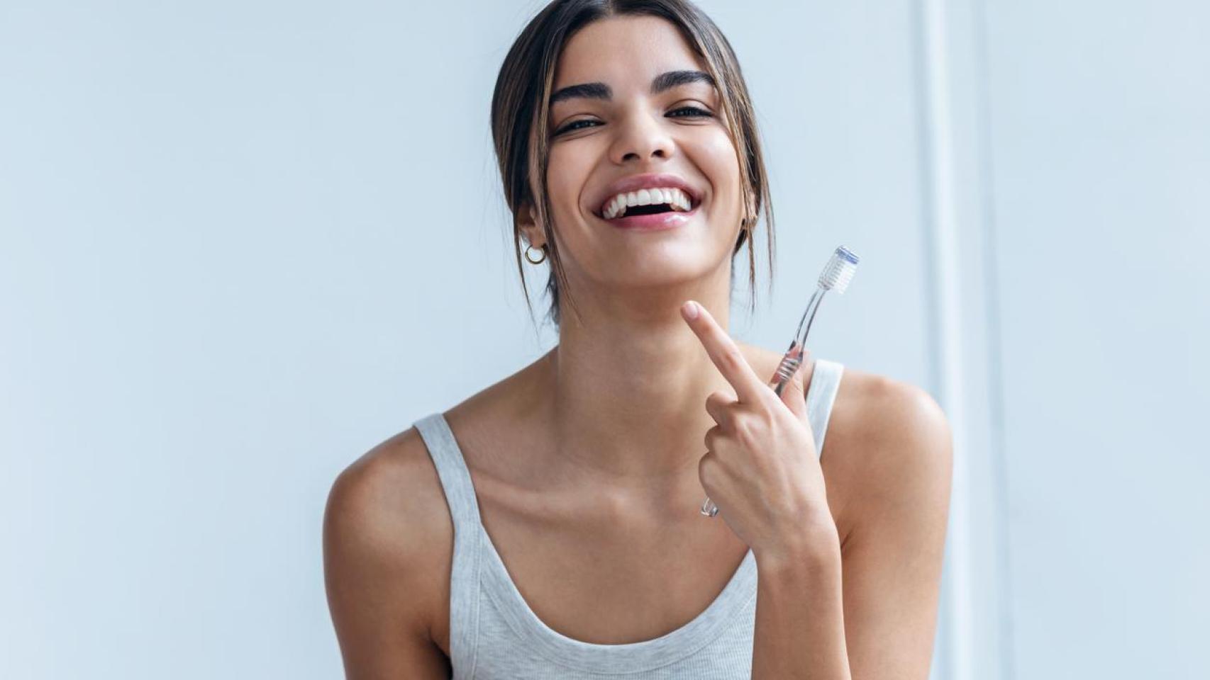 Mujer sonriente señalándose los dientes después de habérselos lavado.