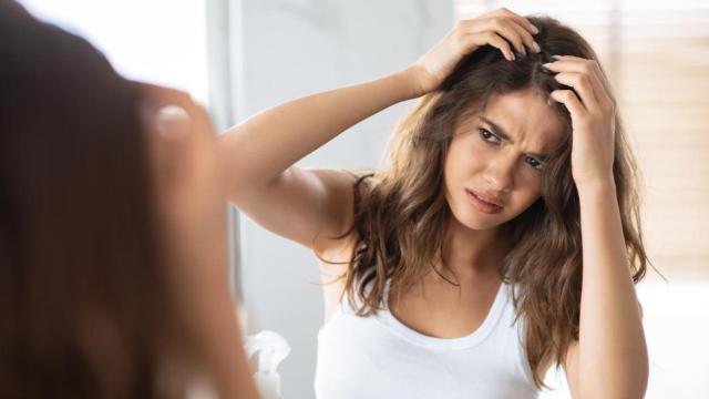 Mujer buscándose canas frente al espejo.