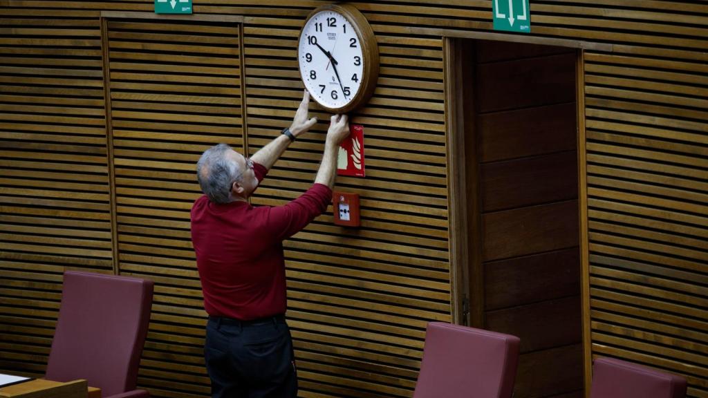 Un técnico de Les Corts ajuste de reloj del hemiciclo momentos antes del pleno de este viernes en el que el president de la Generalitat comparece para explicar la gestión de la DANA. Efe / Ana Escobar