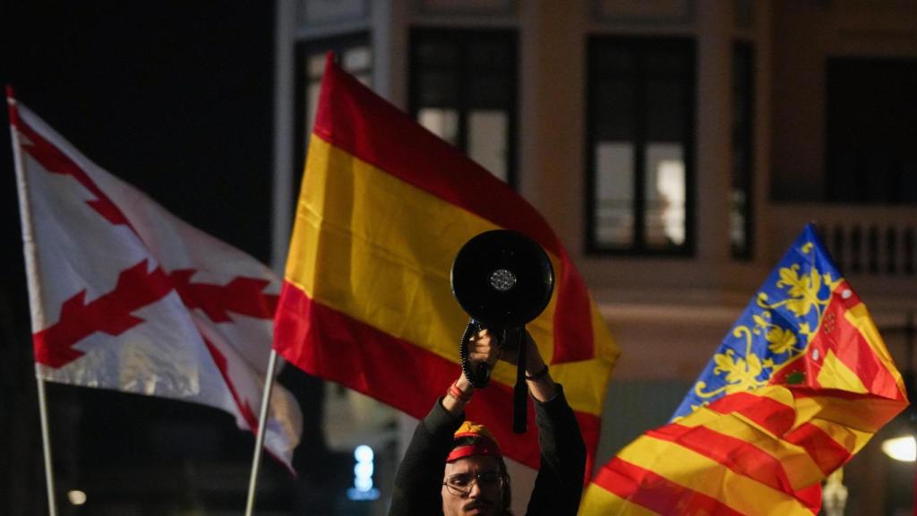 Una persona sostiene un altavoz rodeado de banderas, durante una manifestación contra Sánchez y Mazón, en la Plaza de San Agustín, Valencia.