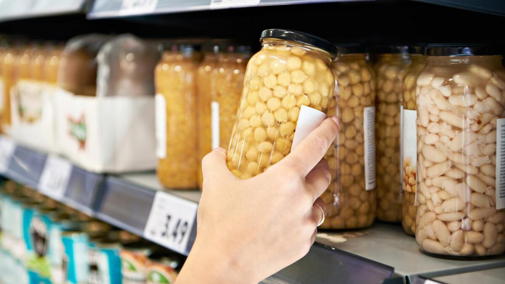 Una persona coge un bote de garbanzos en un supermercado.