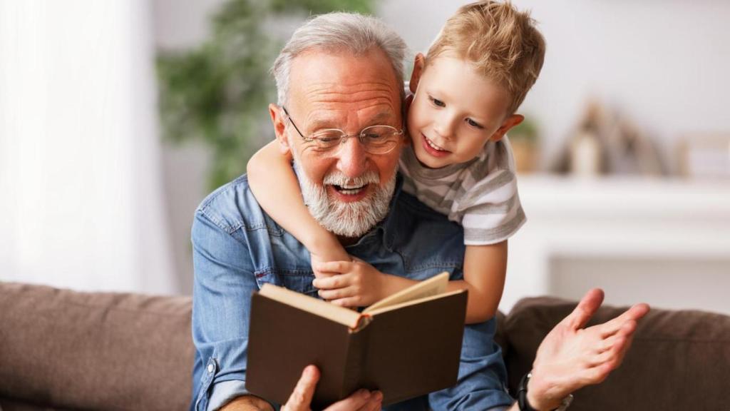 Un abuelo alegre leyendo un libro junto a su nieto.