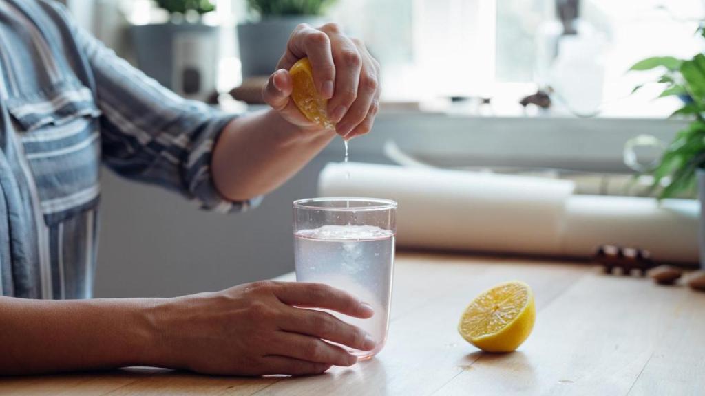 Mujer exprimiendo medio limón en un vaso de agua