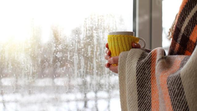 Mujer mirando por la ventana en un día de nieve y frío.