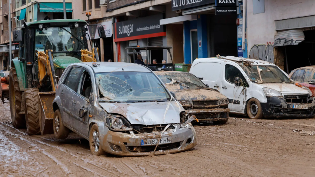 Una máquina excavadora retira vehículos amontonados en una calle de Alfafar.