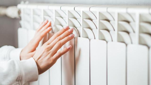 Una mujer calienta sus manos frente a un radiador encendido.