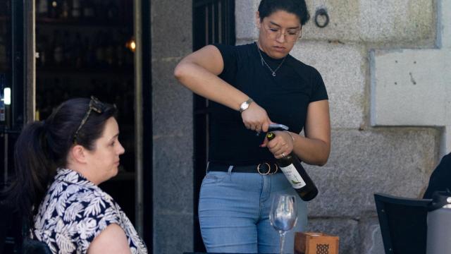 Una camarera abre una botella de vino.