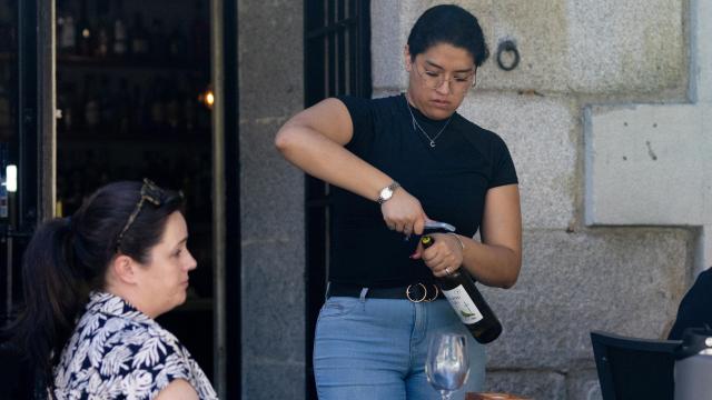 Una camarera abre una botella de vino.