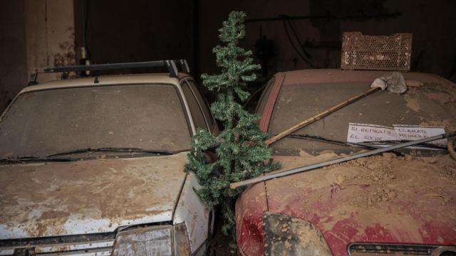 Un árbol de Navidad entre dos coches en un garaje de Paiporta