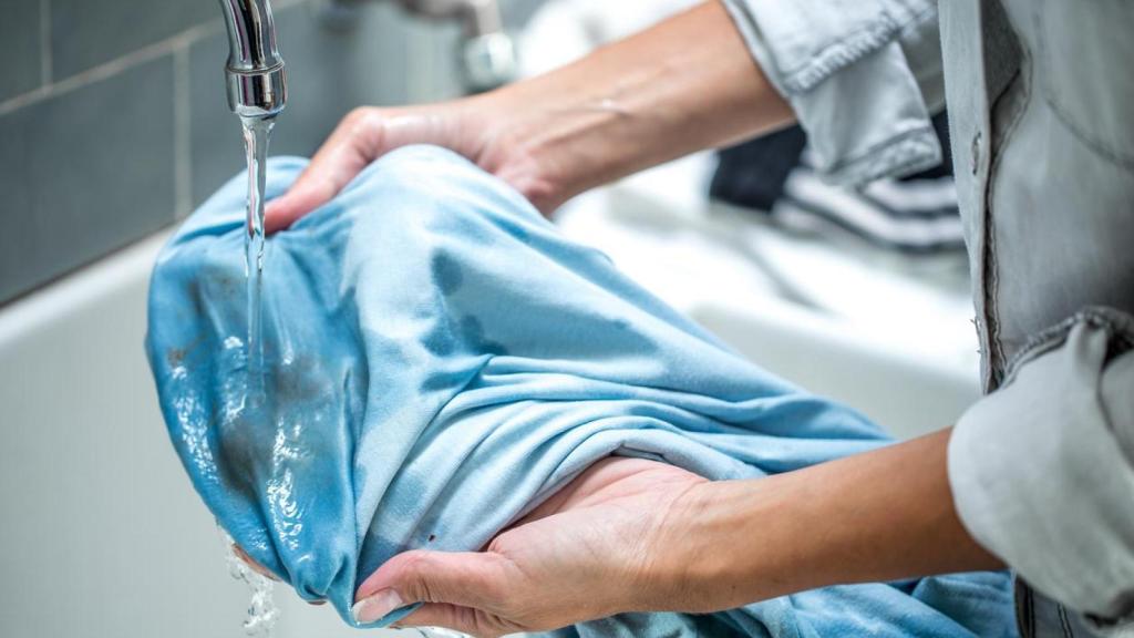 Mujer limpiando una camisa con manchas en el lavabo.