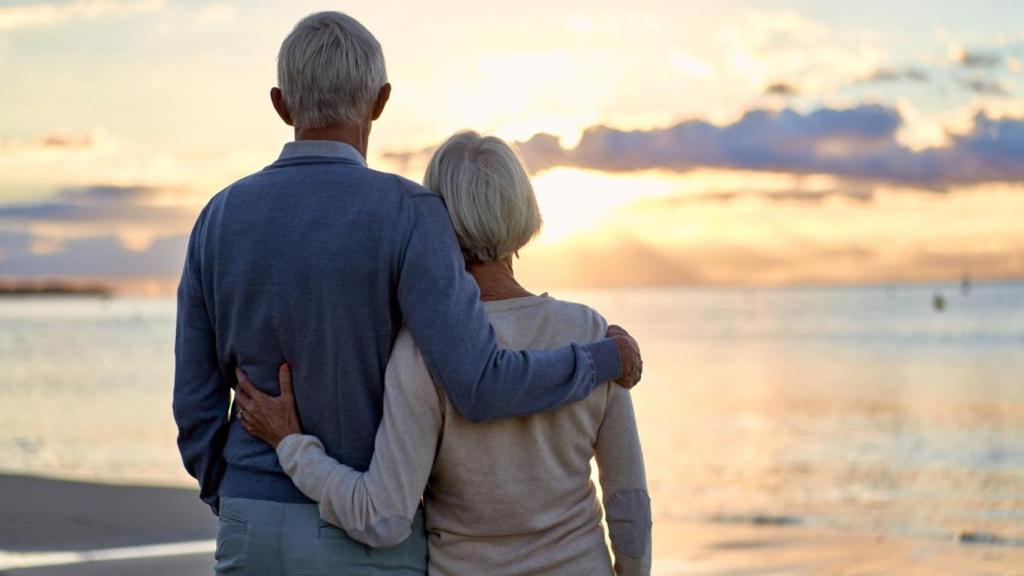 Imagen de una pareja sénior viendo el atardecer en la playa.