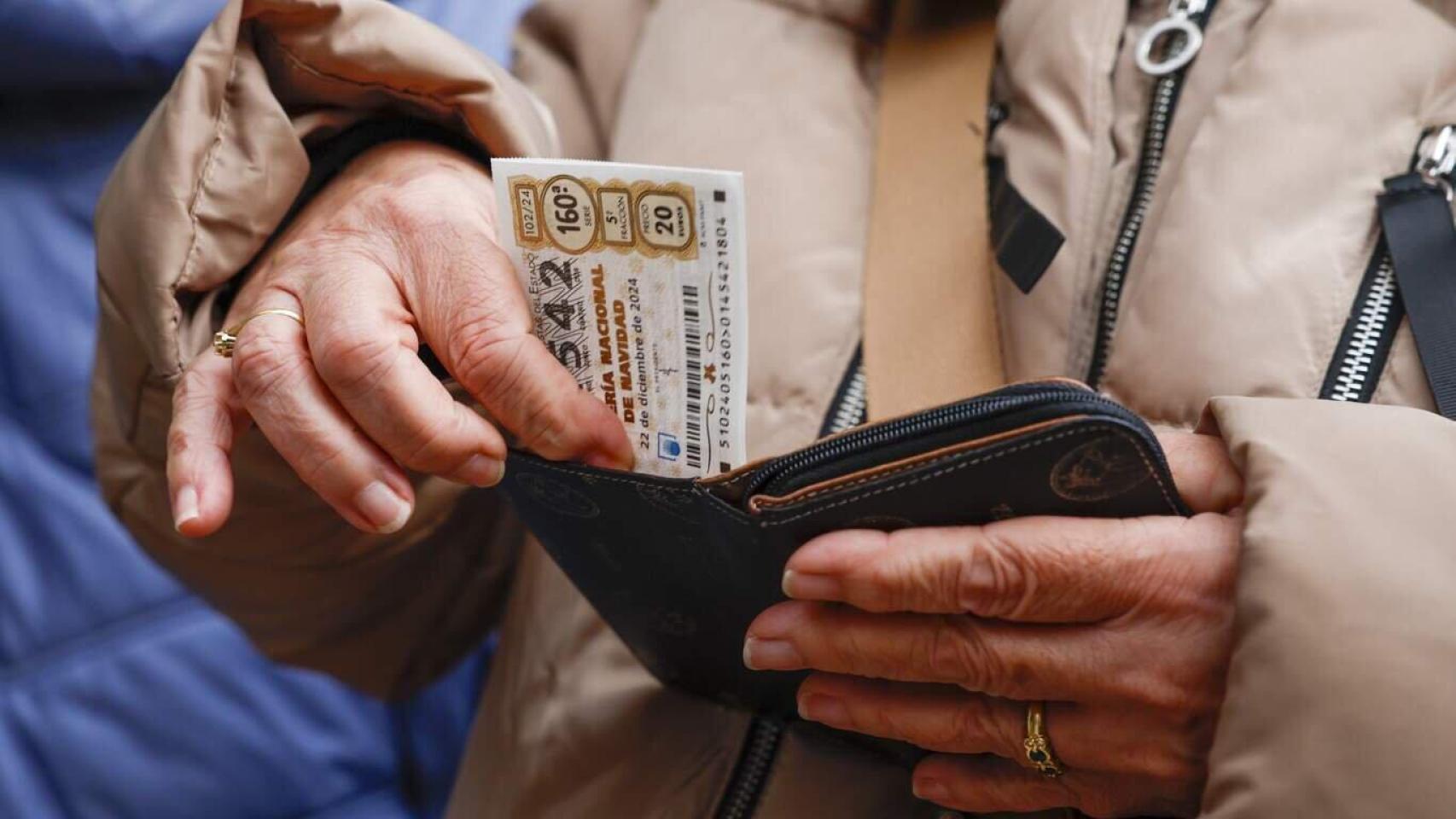 Una persona guardando un décimo de Lotería de Navidad en su cartera.