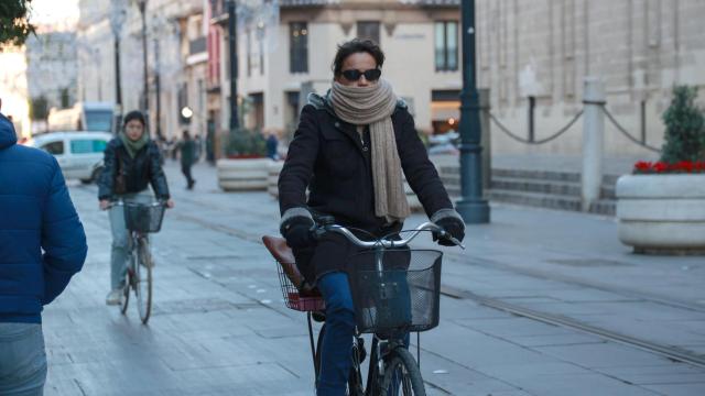 Una mujer se protege del frío con bufanda mientras circula en bicicleta por la Avenida de la Constitución de Sevilla.