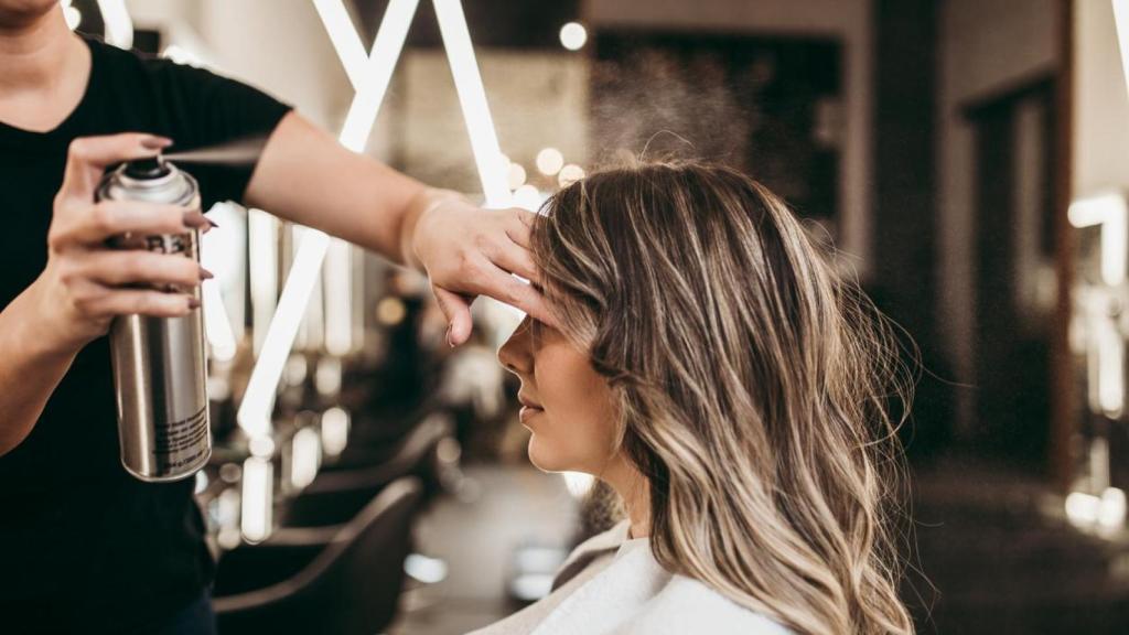 Estilista aplicando laca a una mujer en la peluquería