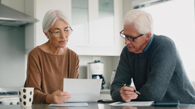 Una pareja de jubilados observando un documento en la cocina de una casa.